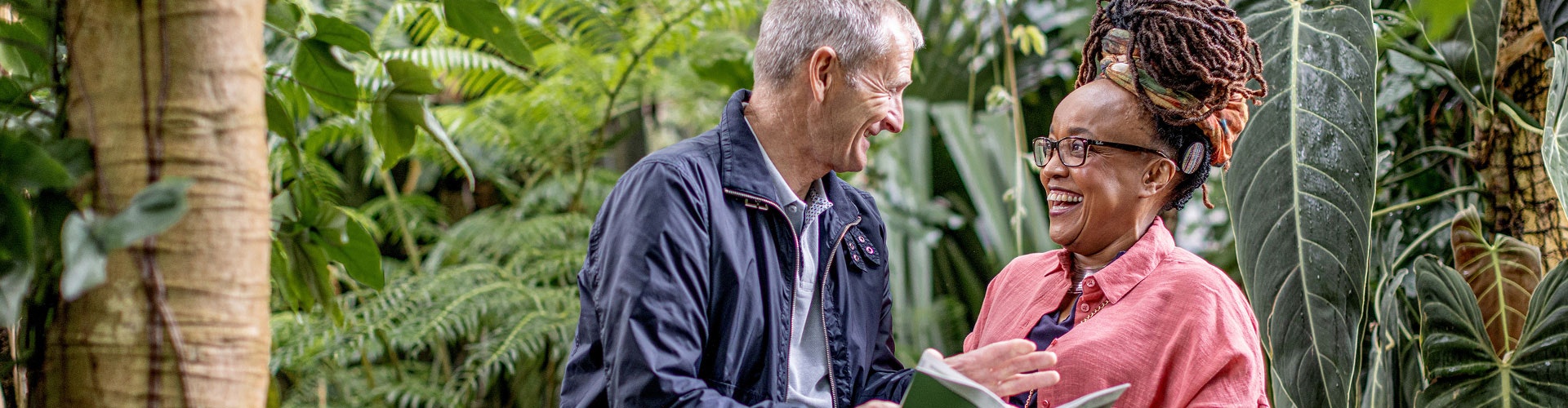 Two people in a garden, talking and holding a document; one is a cochlear implant user.