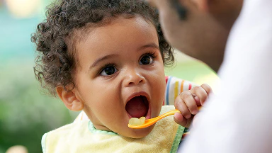 A man feeding his baby outdoors.