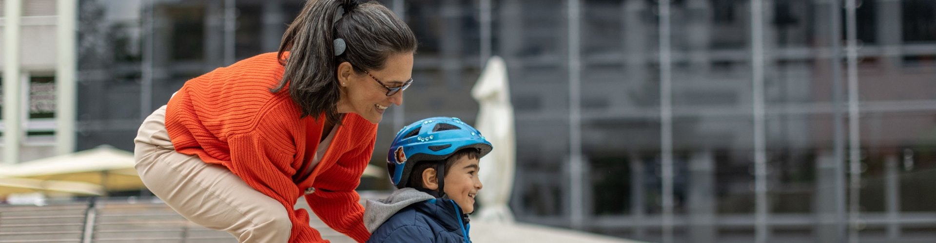 Eine Frau, die einem Buben beim Skateboarden hilft, kann dank ihres Cochlea-Implantats sein Lachen hören.