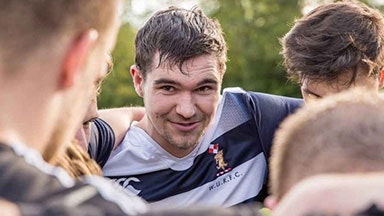 En gruppe rugbyspillere samlet seg på en idrettsplass med våpen rundt hverandre.