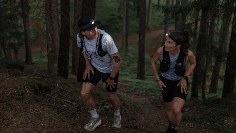 A man and a woman hiking in the woods in the evening with a headlamp
