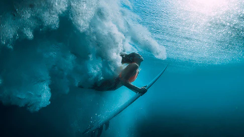 Woman on a surf board diving under breaking wave