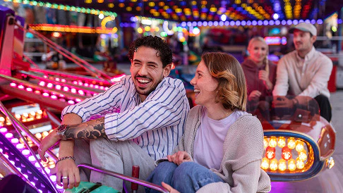 A man and a woman enjoying a fairground ride with colorful lights in the background