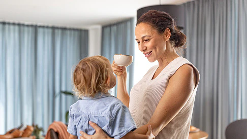 Mother drinking a coffee while cuddling with her toddler