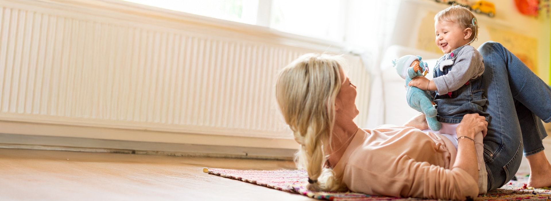 Parent and child (less than a year) lay on the floor looking at each other. The child has an cochlear implant
